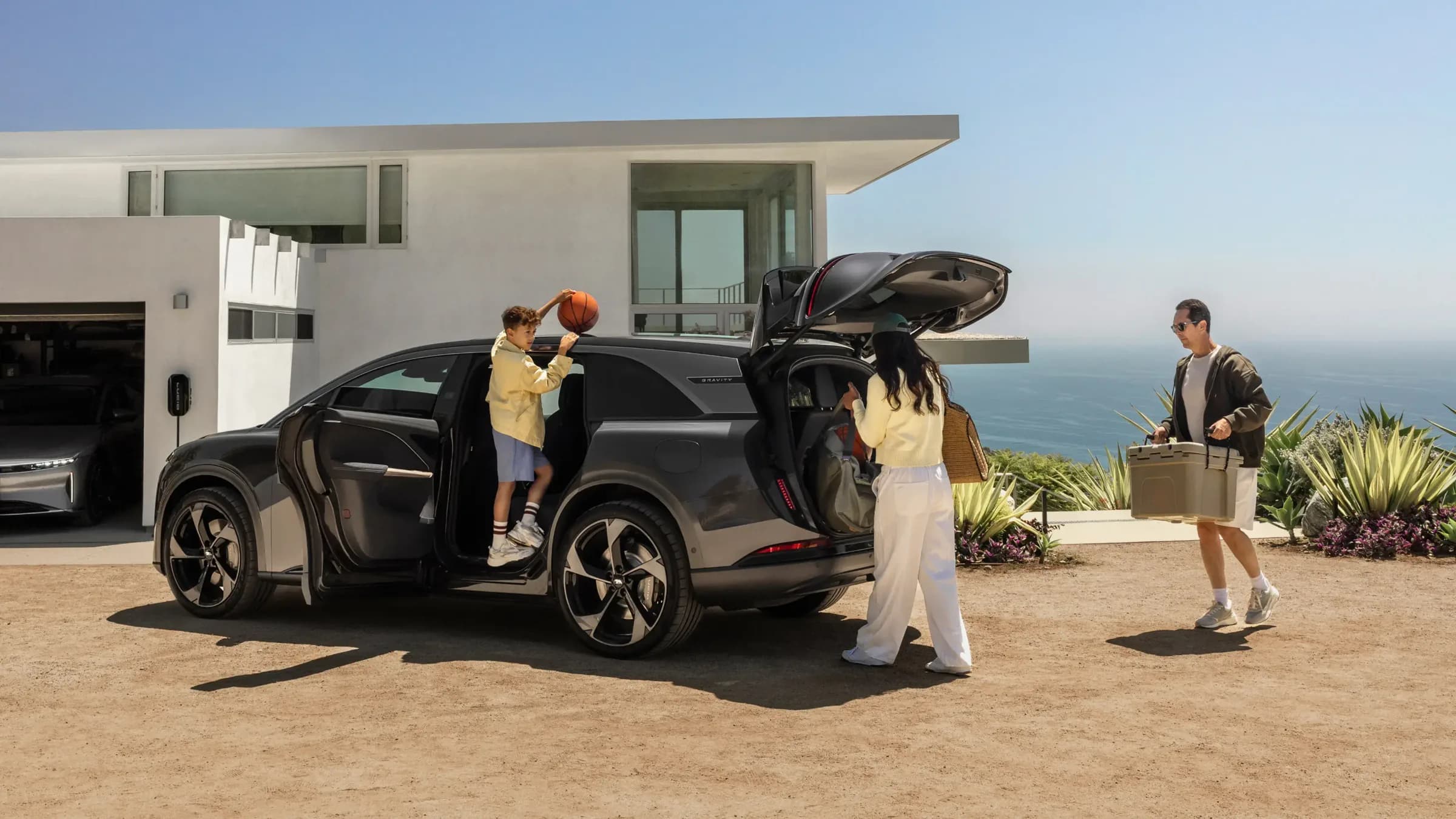 Gia đình đang chất đồ lên chiếc SUV màu xám đậm trước một ngôi nhà ven biển hiện đại.